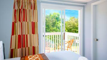Quarto com uma cama, vista para uma varanda com cadeiras e uma janela com cortinas.