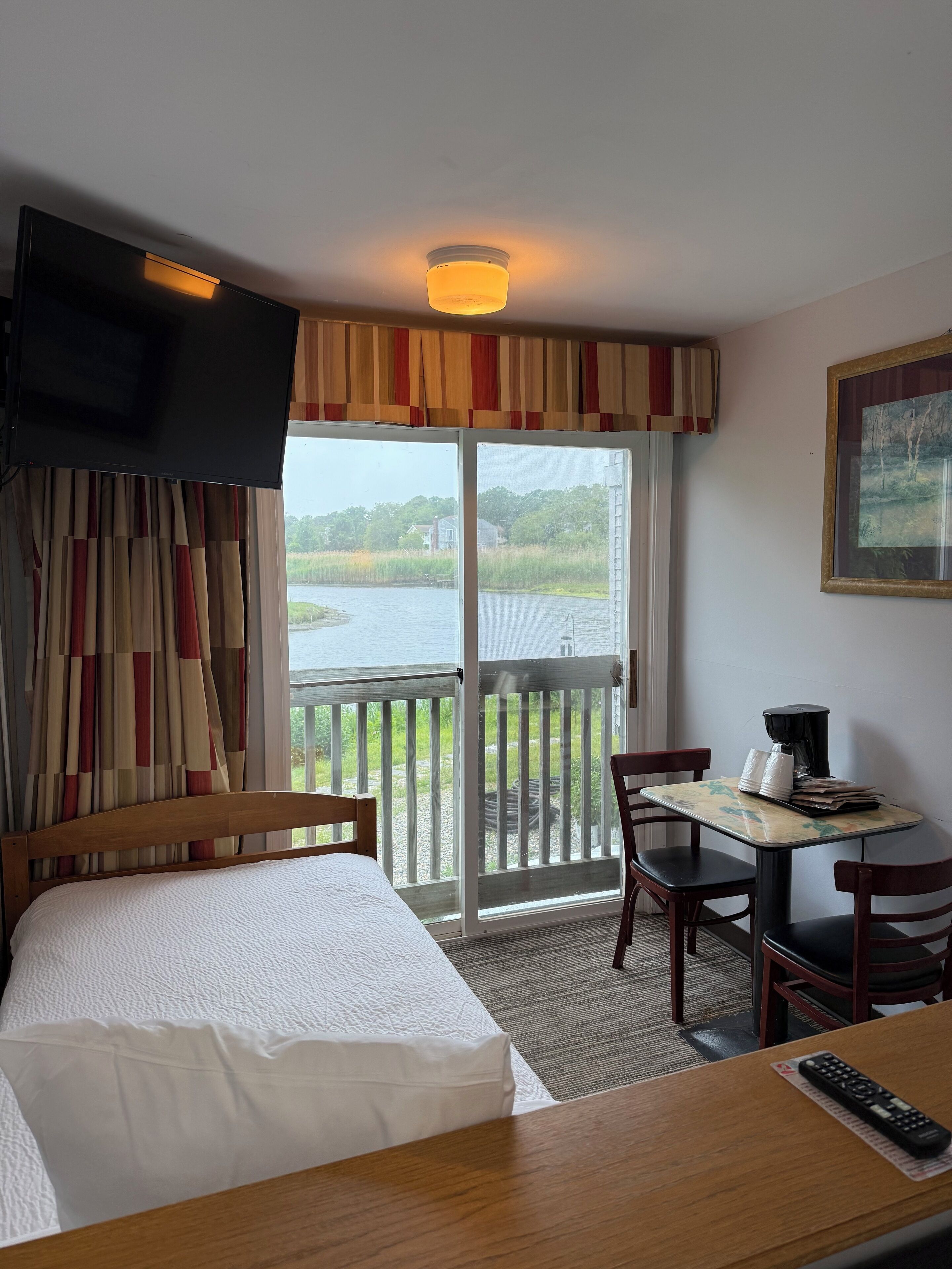 Habitación de hotel con cama, escritorio con cafetera, televisor montado en la pared y vista al lago a través de la ventana.