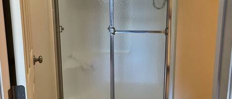 A glass-enclosed shower stall with a showerhead, a door with a handle, and a tiled floor.
