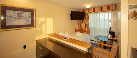 Una habitación de hotel con una cama, un escritorio, una silla, un televisor y un cuadro en la pared.