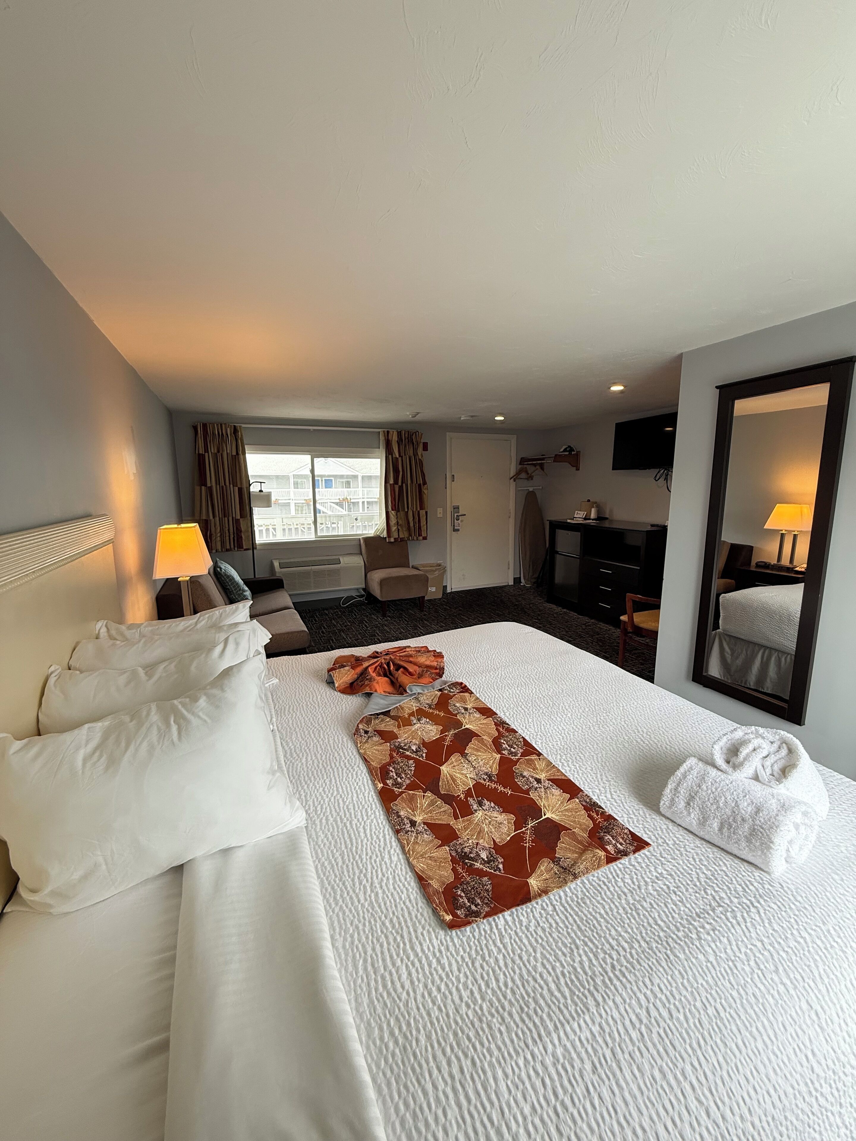 A hotel room with a large bed, a TV, a desk, and a window with curtains.
