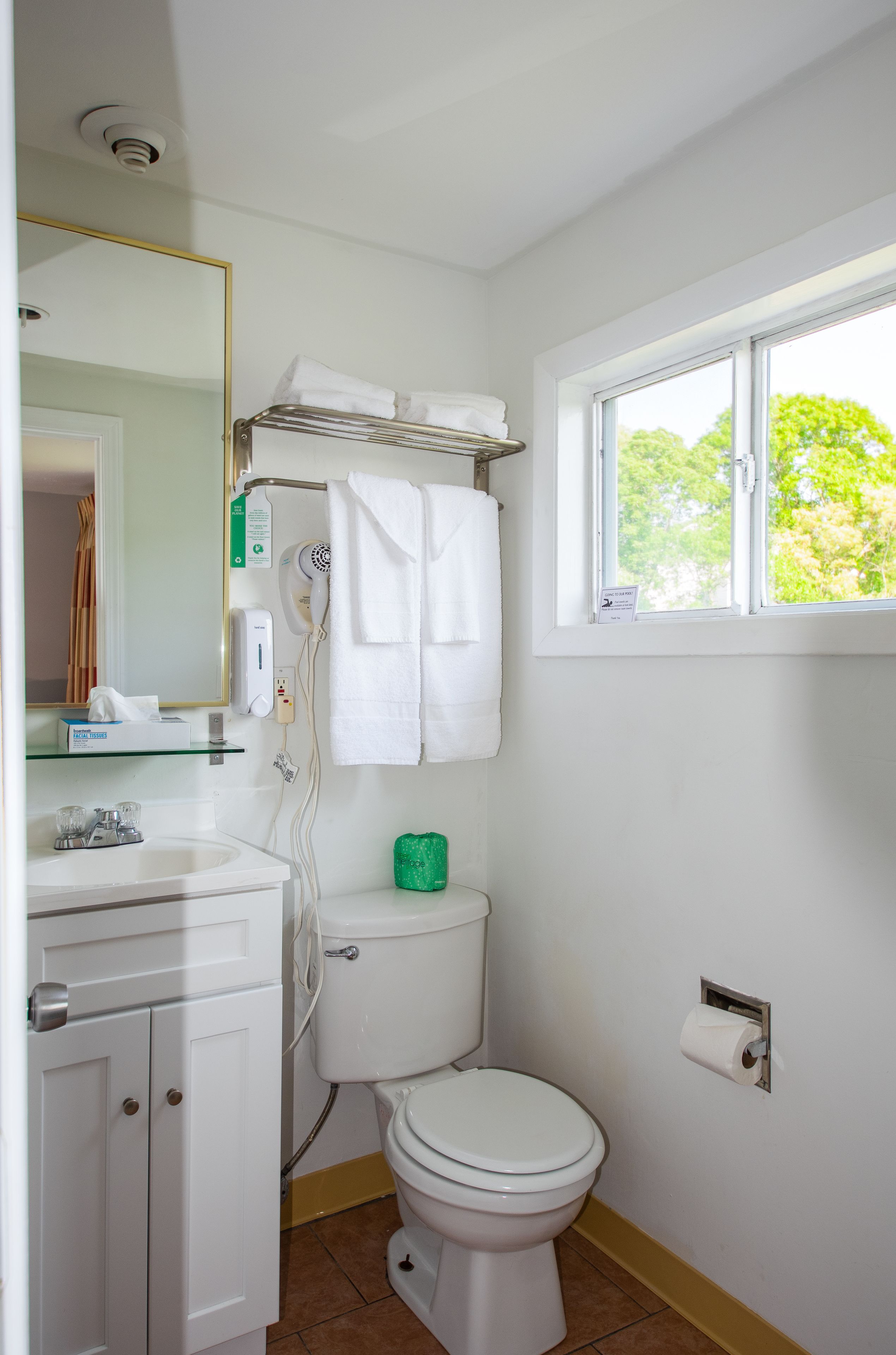 Un baño con inodoro, lavamanos y ventana con vistas a árboles.