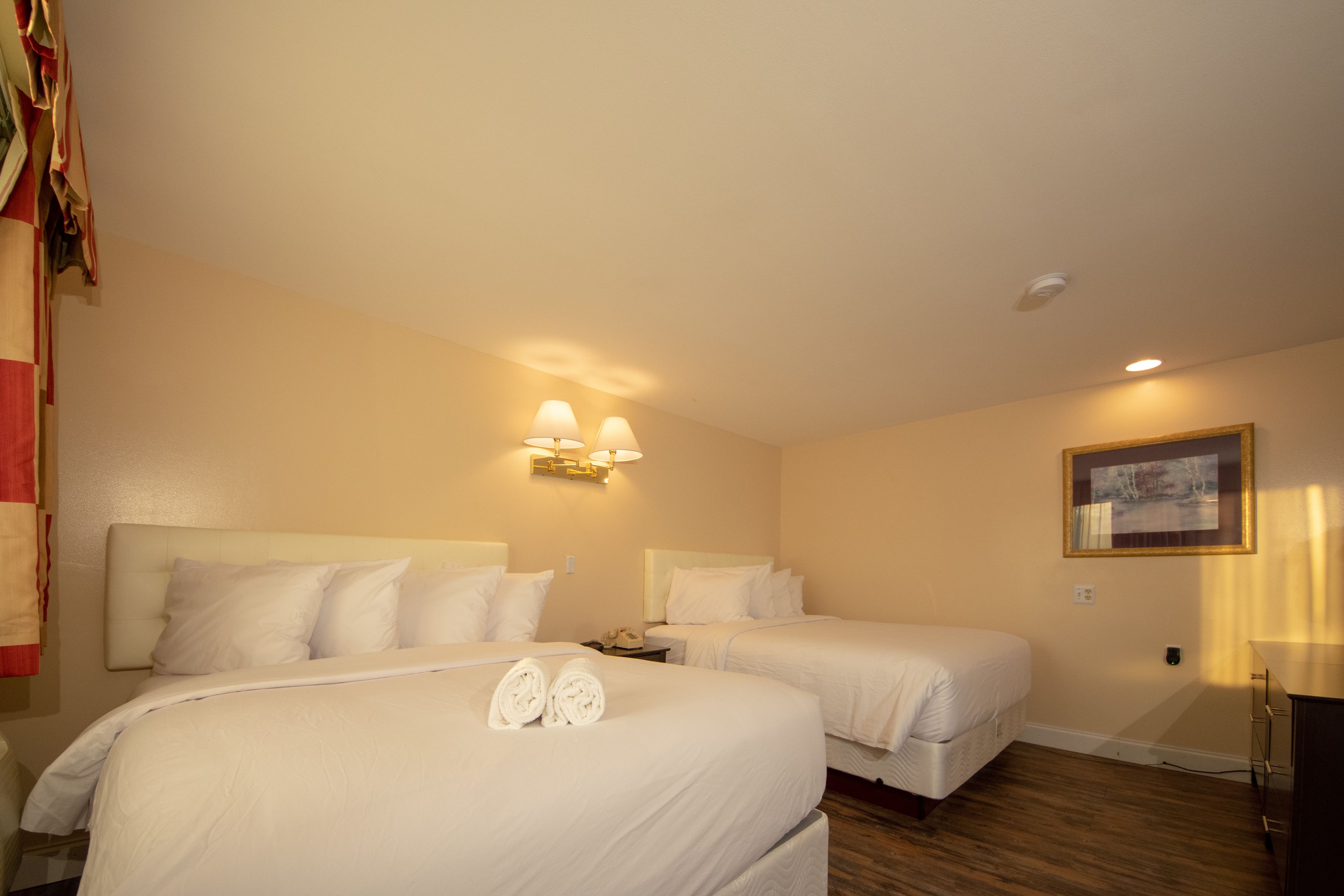 A hotel room with two beds, a nightstand, a desk, and a painting on the wall.