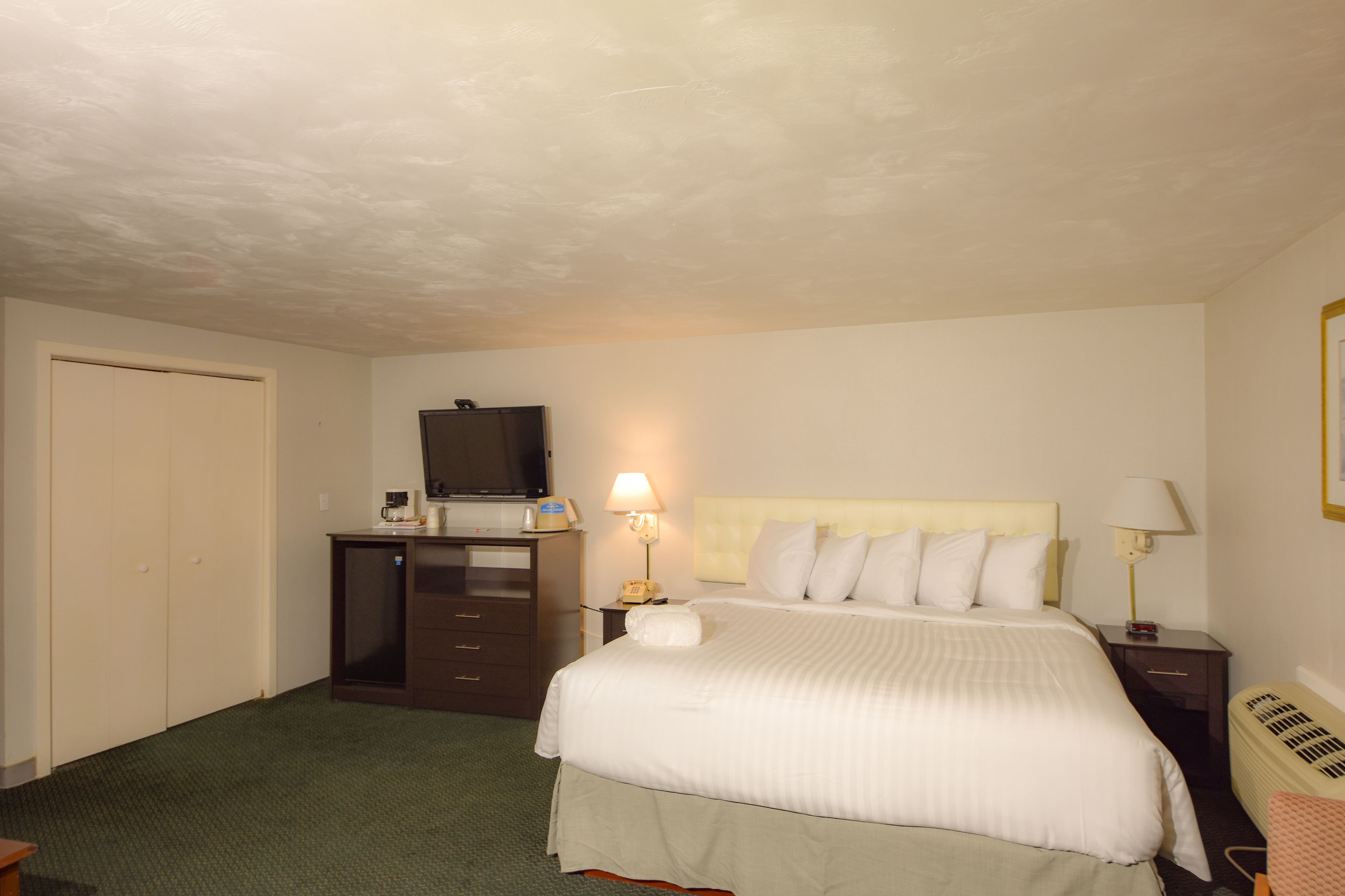 A hotel room with a bed, a desk with a computer, a television, and a lamp.