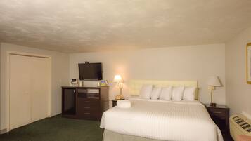 Quarto de hotel com uma cama, uma escrivaninha com computador, televisão e abajur.
