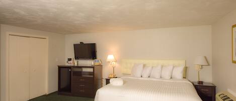 A hotel room with a bed, a desk with a computer, a television, and a lamp.