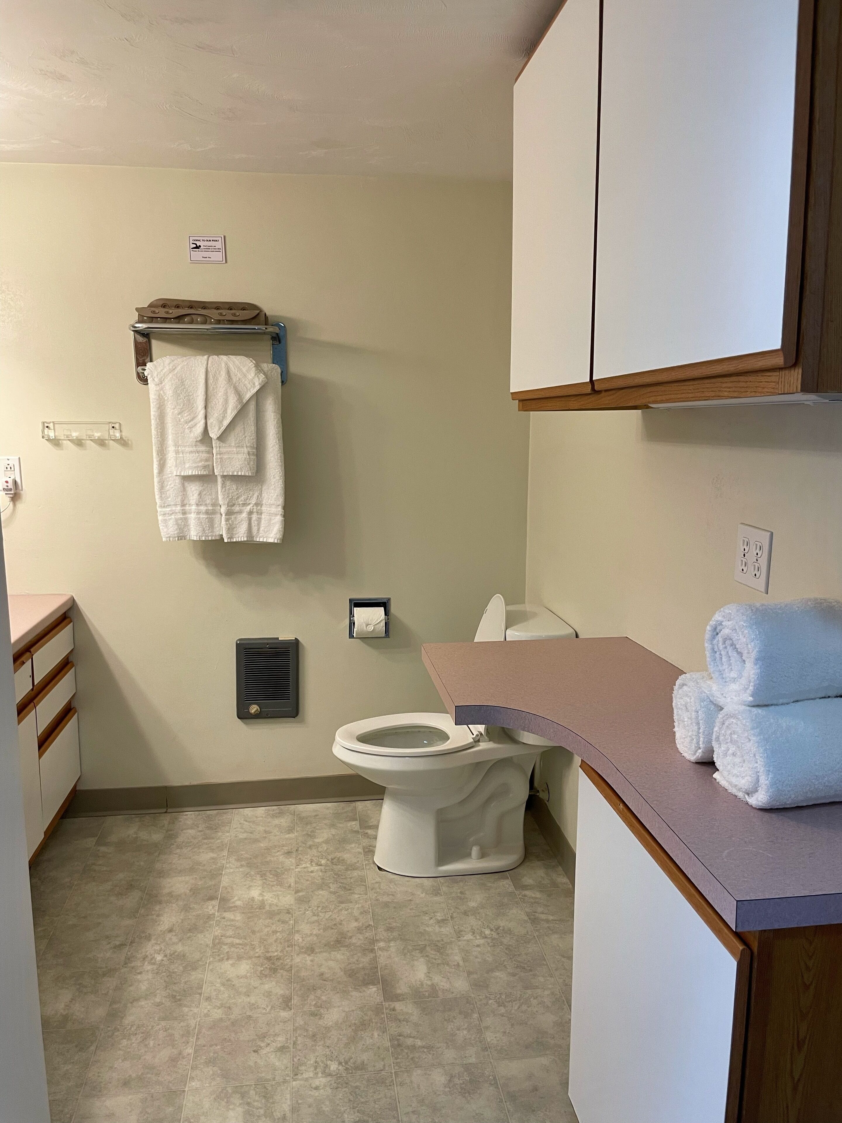 Un baño con inodoro, toallero con toallas, dispensador de toallas y un armario.