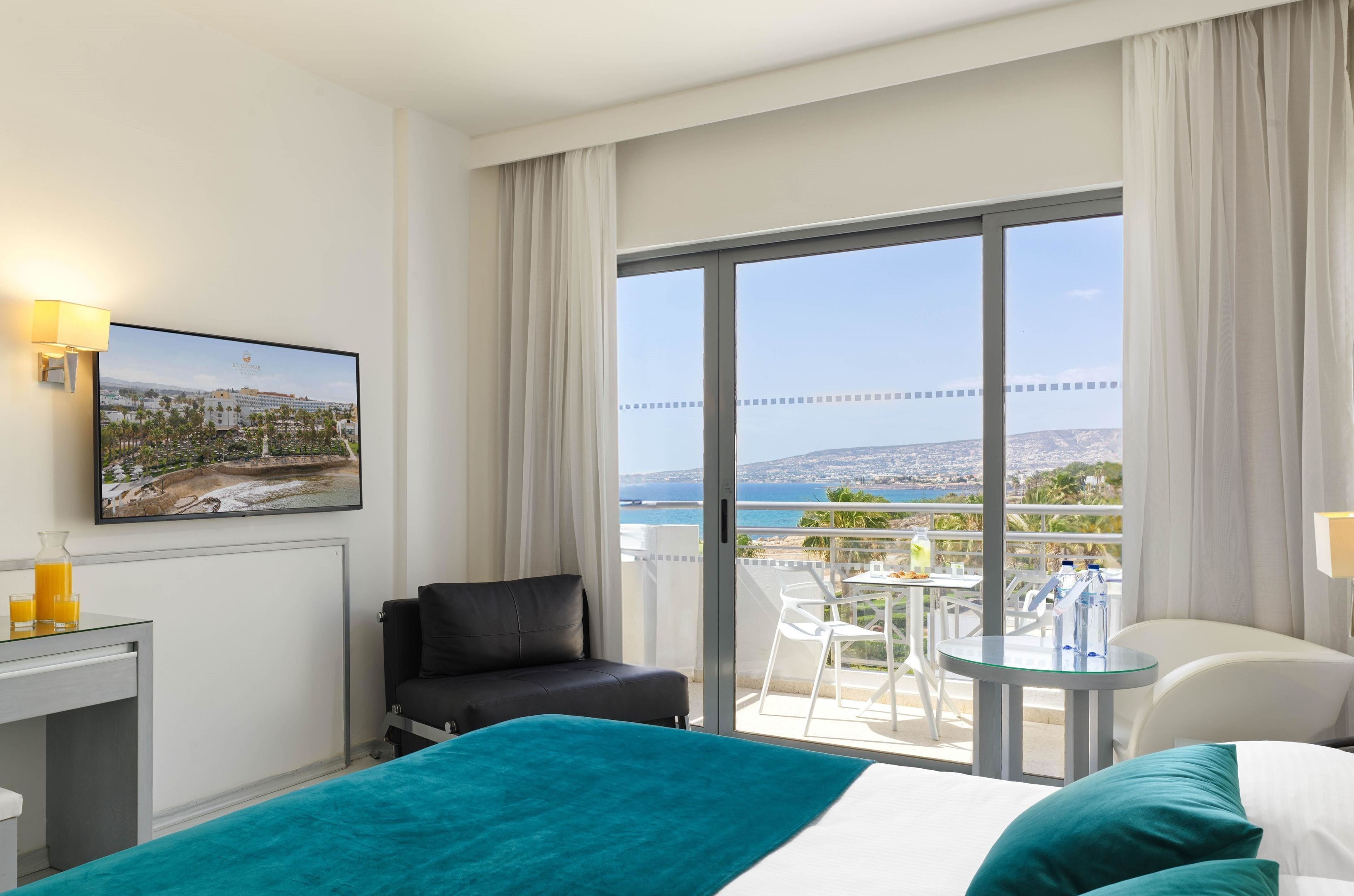 Habitación de hotel con cama, escritorio con lámpara, silla y balcón con mesa y sillas.