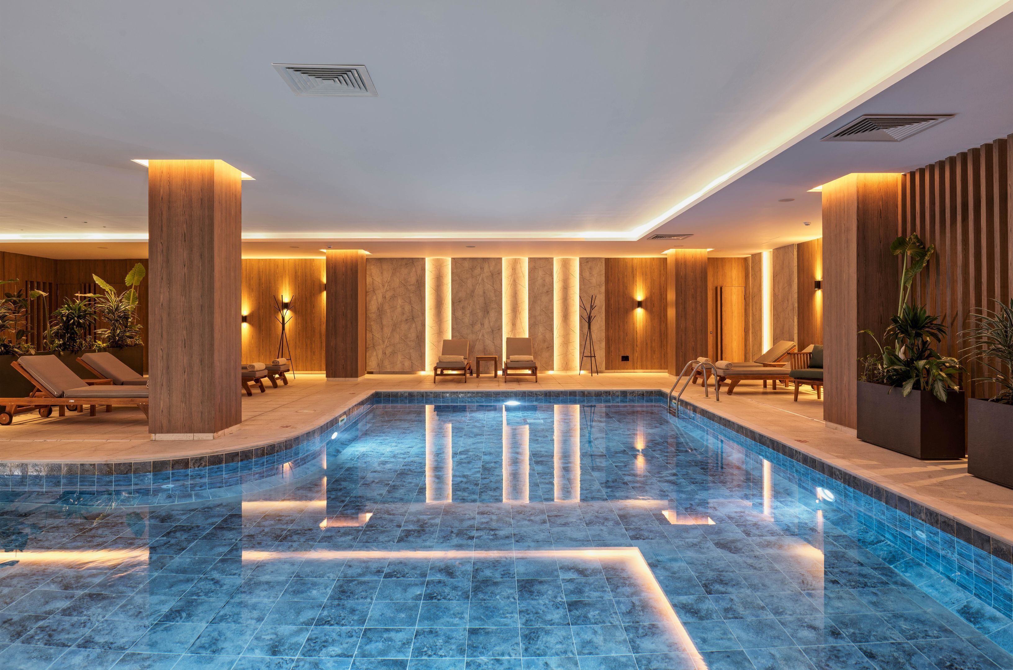 Una piscina interior moderna con sillas de descanso y detalles de madera.