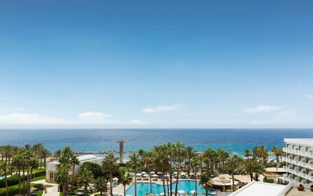 A resort with a pool, palm trees, and a view of the ocean.