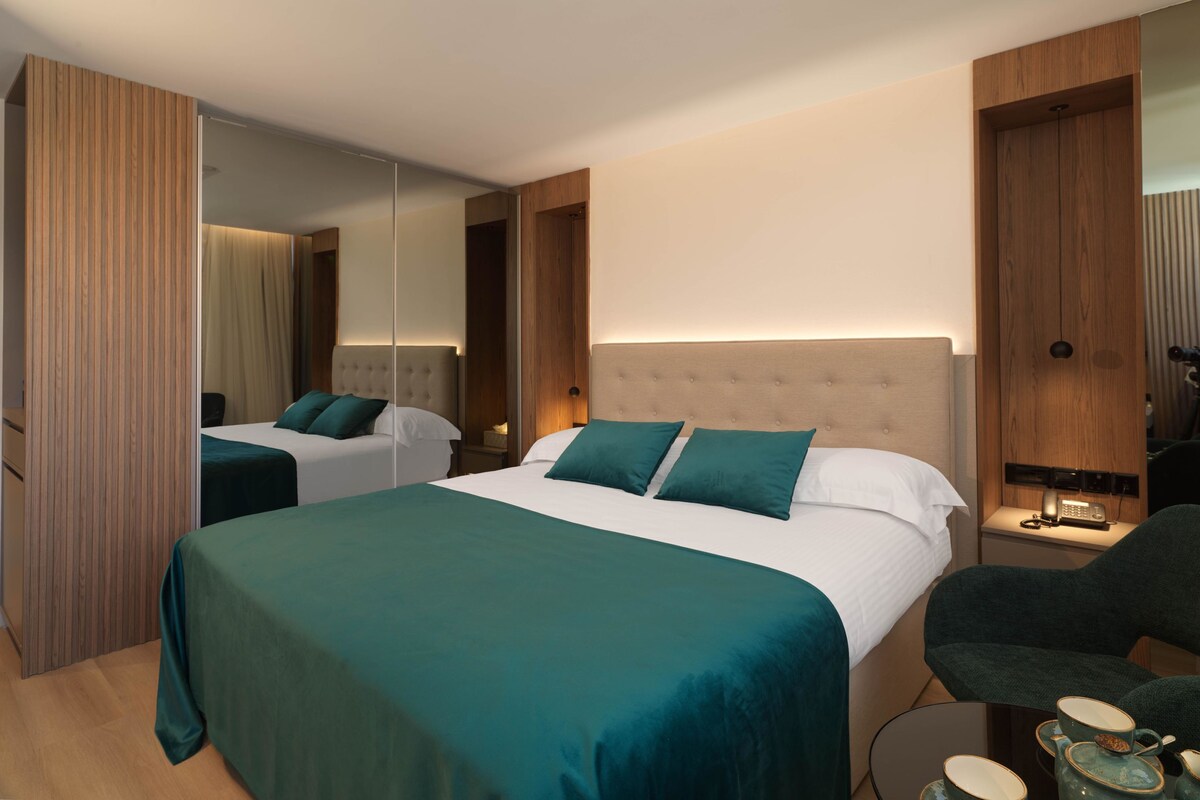 Habitación de hotel con dos camas, zona de estar y espejo.