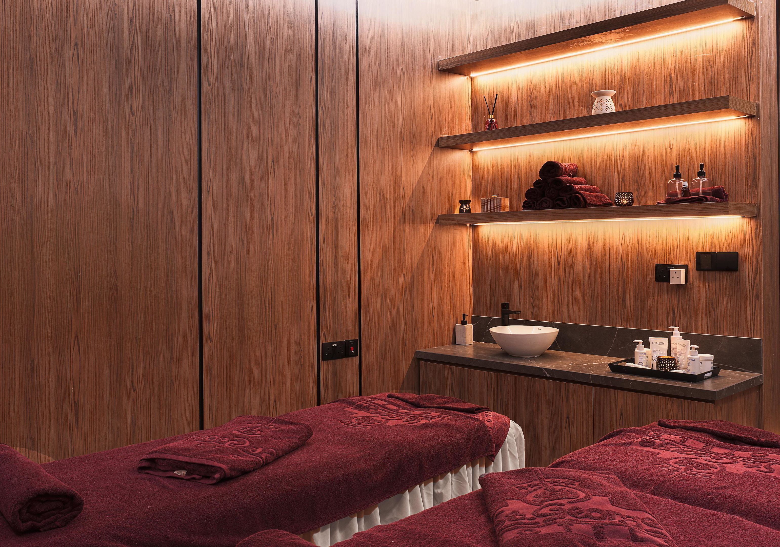 Un cuarto de spa con paneles de madera, un lavabo y dos camillas para masajes con toallas rojas.
