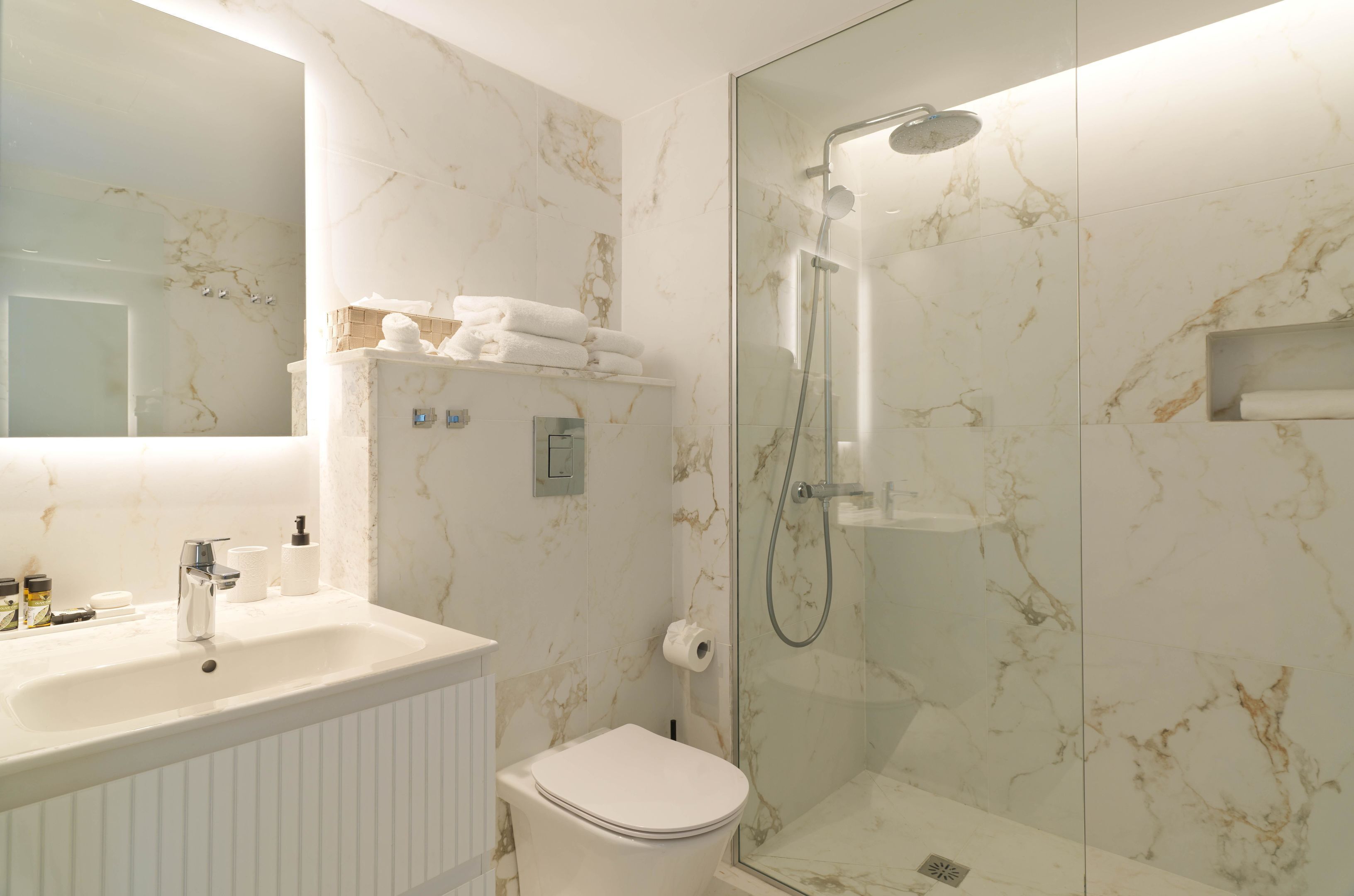 Een badkamer met een marmeren wand, een douche met glazen wanden, een witte wastafel en een toilet.
