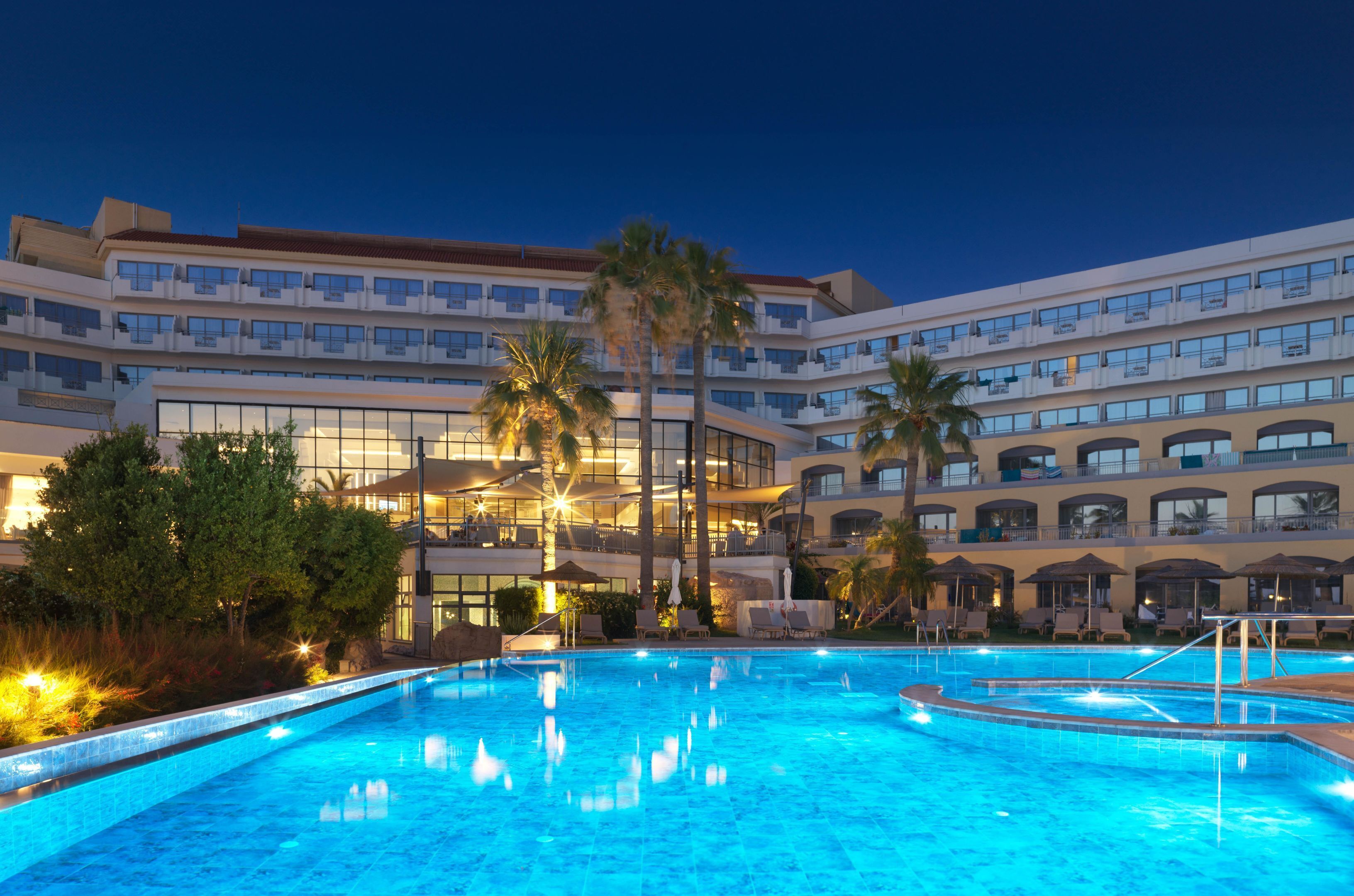 A hotel with a large swimming pool, palm trees, and a multi-story building with balconies.
