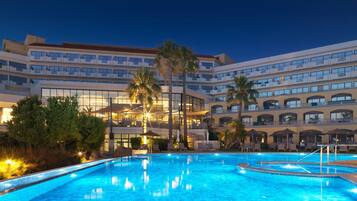 A hotel with a large swimming pool, palm trees, and a multi-story building with balconies.