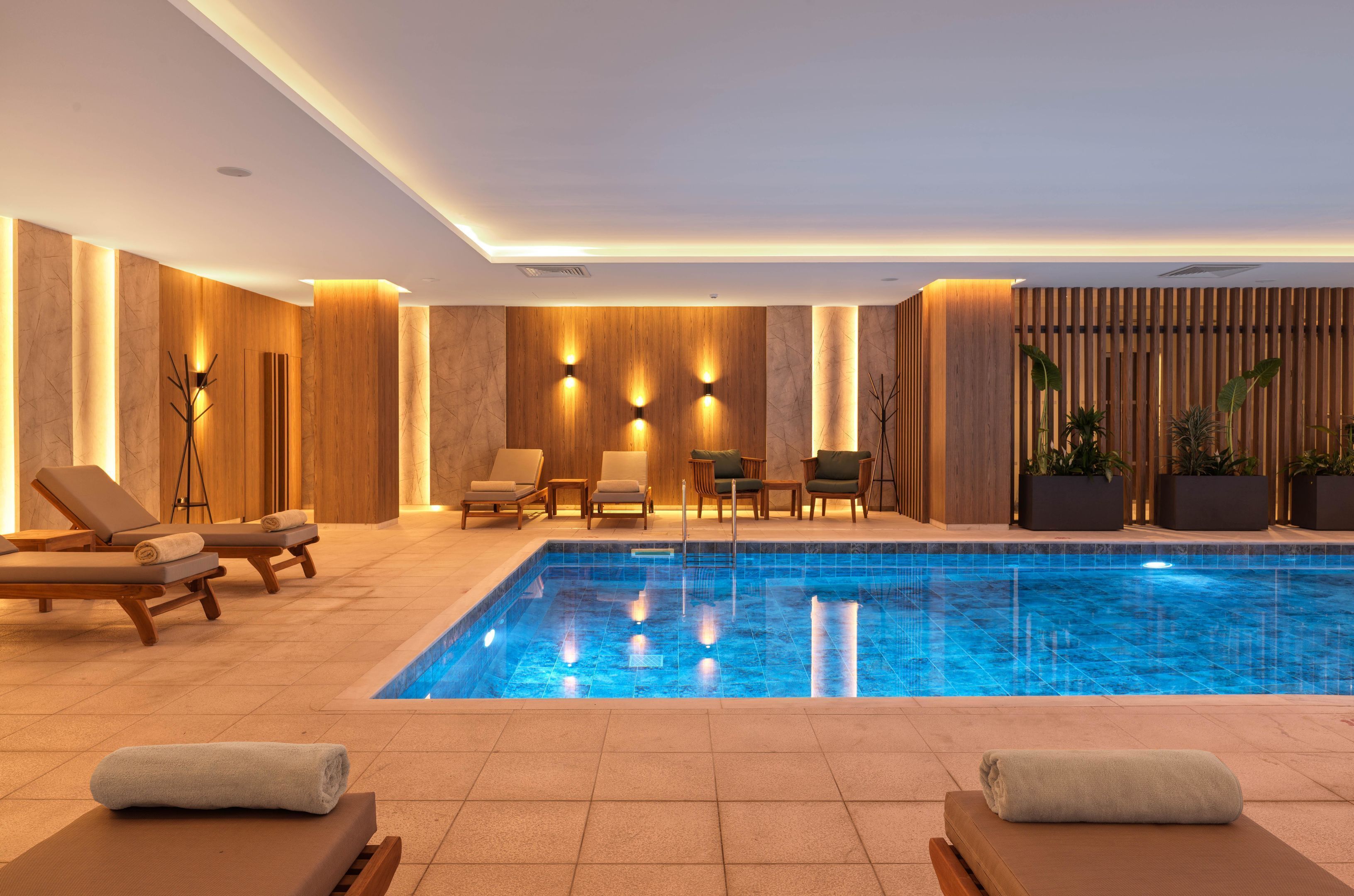 Un área interior de piscina moderna con sillones reclinables y un espacio de descanso.