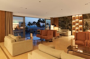 Un moderno hall de hotel con un amplio espacio de descanso, una chimenea y una pared de botellas iluminadas.