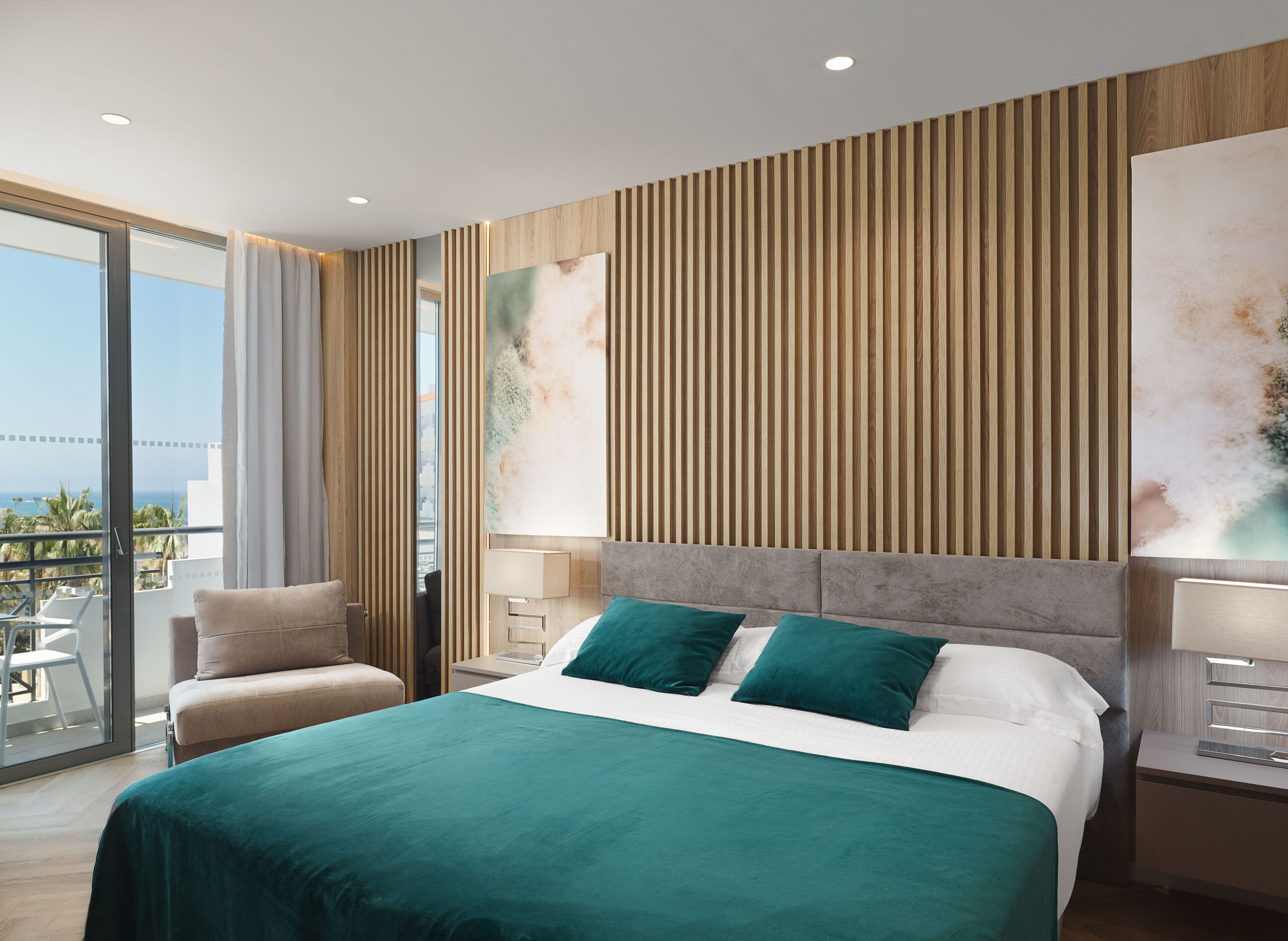 Une chambre d’hôtel moderne avec un grand lit, un balcon offrant une belle vue et un grand tableau accroché au mur.
