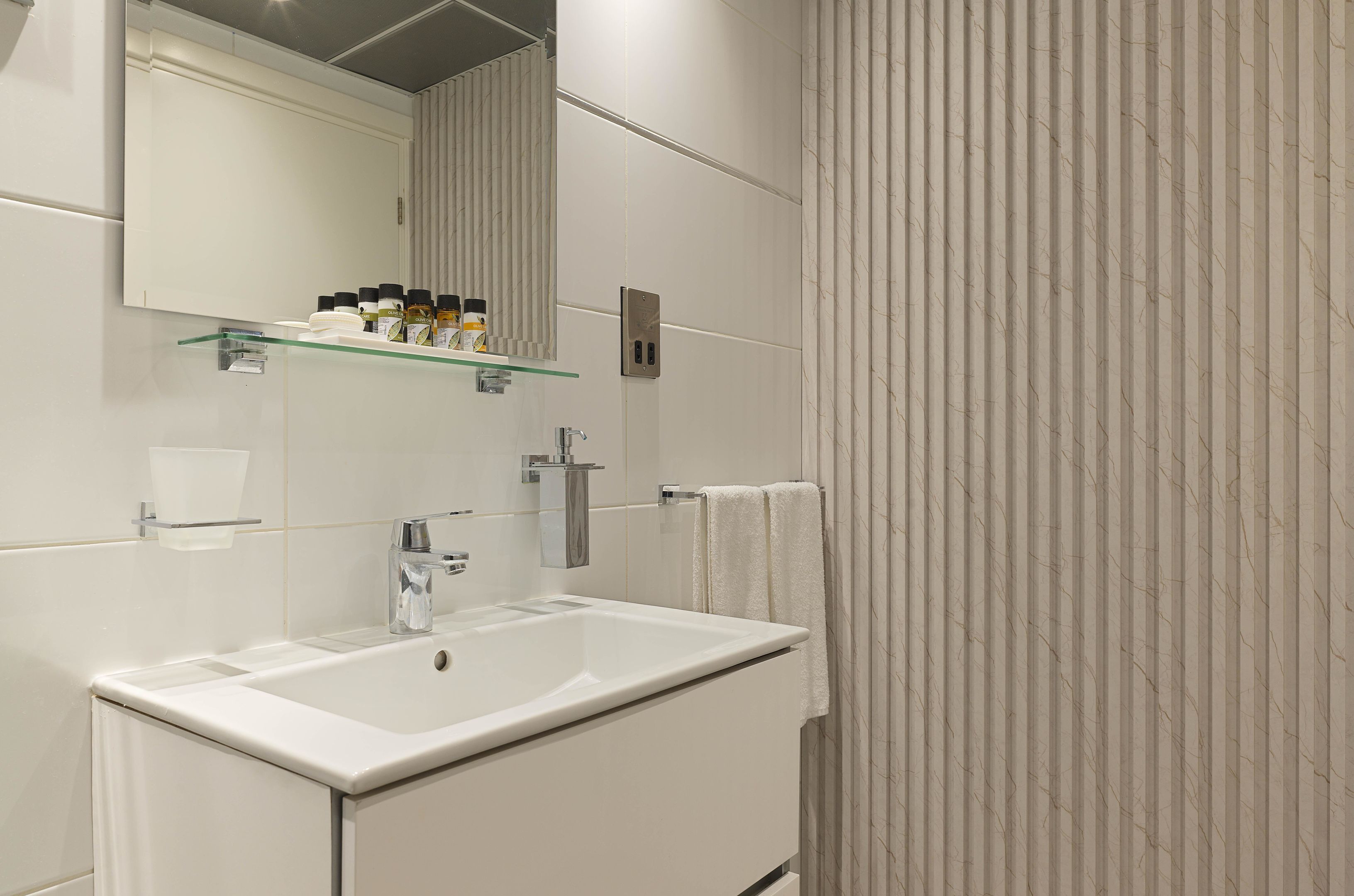 Un baño moderno con un lavamanos grande, espejo y repisa de vidrio con artículos de aseo.