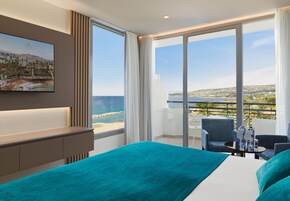 Quarto de hotel com uma cama grande, televisão fixada na parede e varanda com vista para o mar.