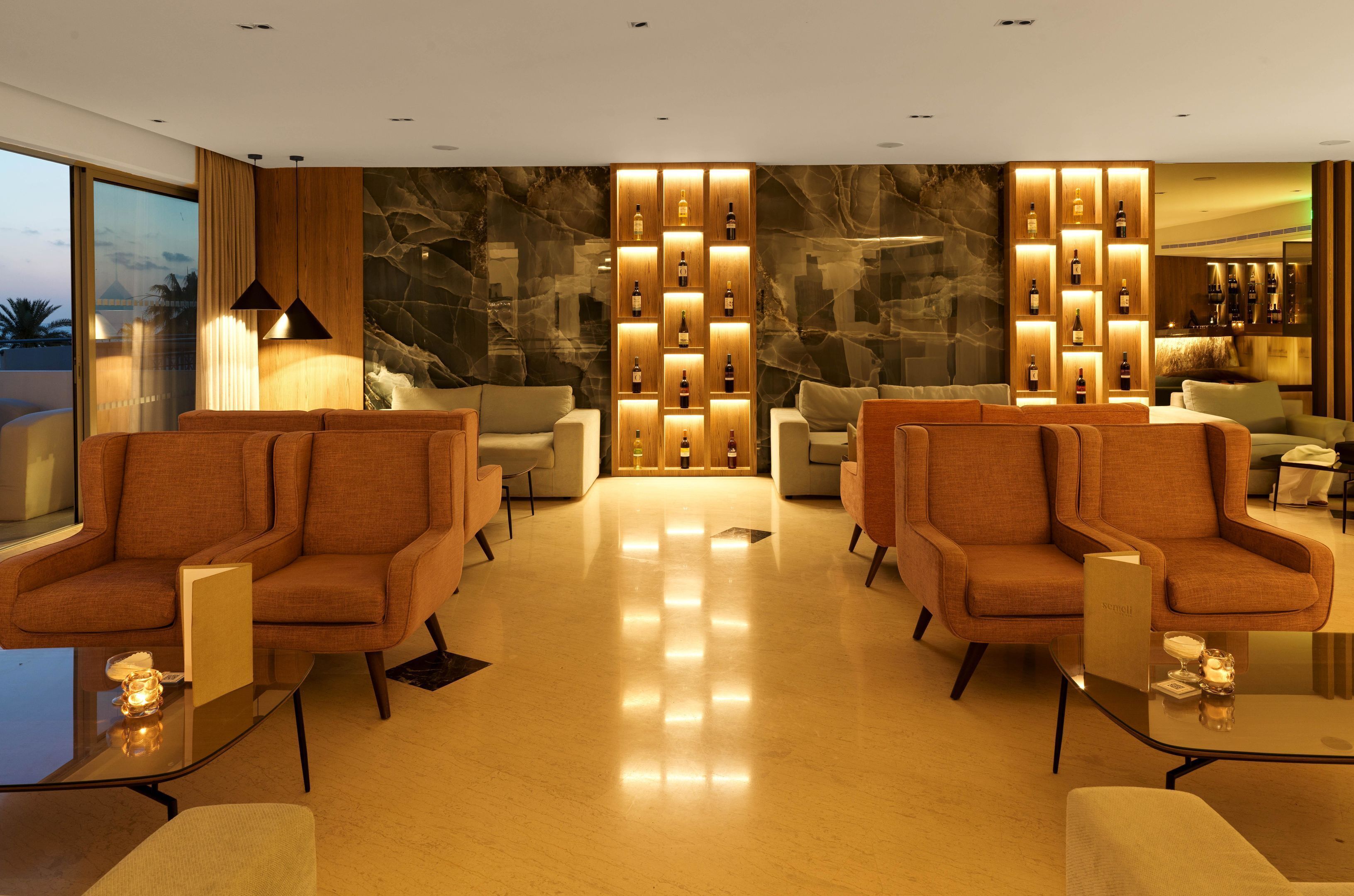 A modern lobby with two sofas, a marble wall, and a wine display.