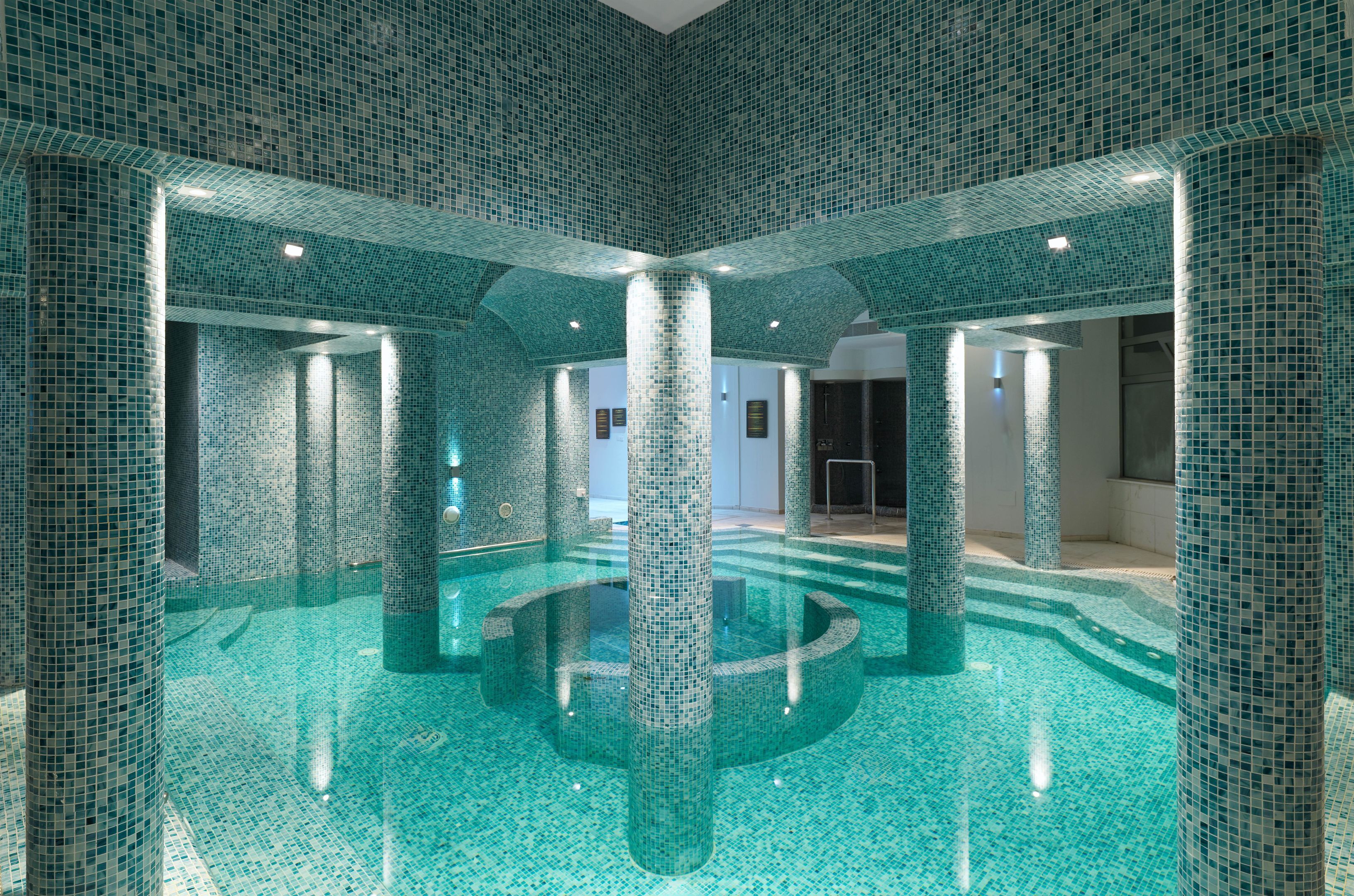 Ein großes Hallenbad mit Fliesenboden und -wänden, umgeben von Säulen.