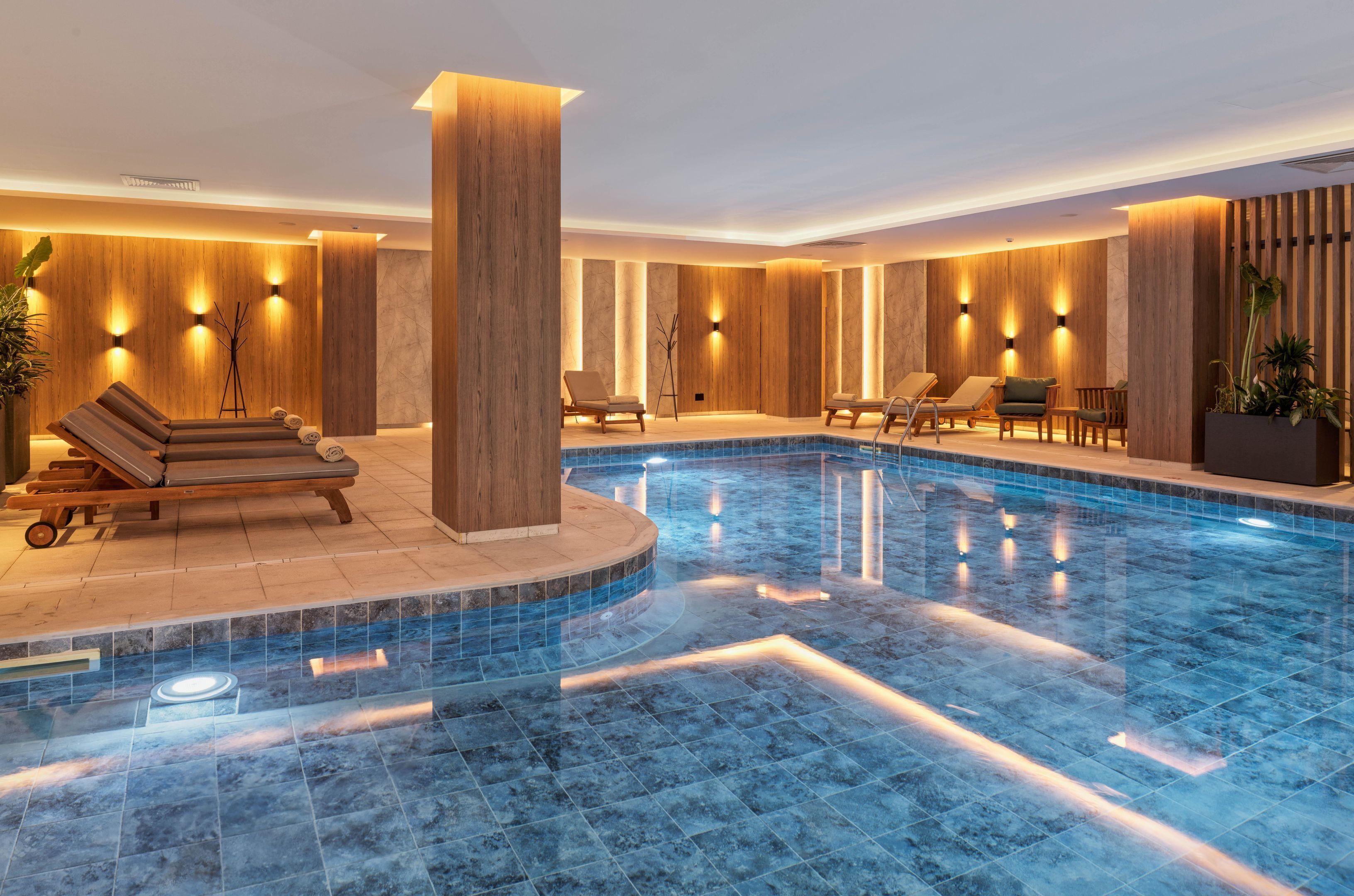 Un área interior de piscina moderna con sillones de descanso y una piscina central.