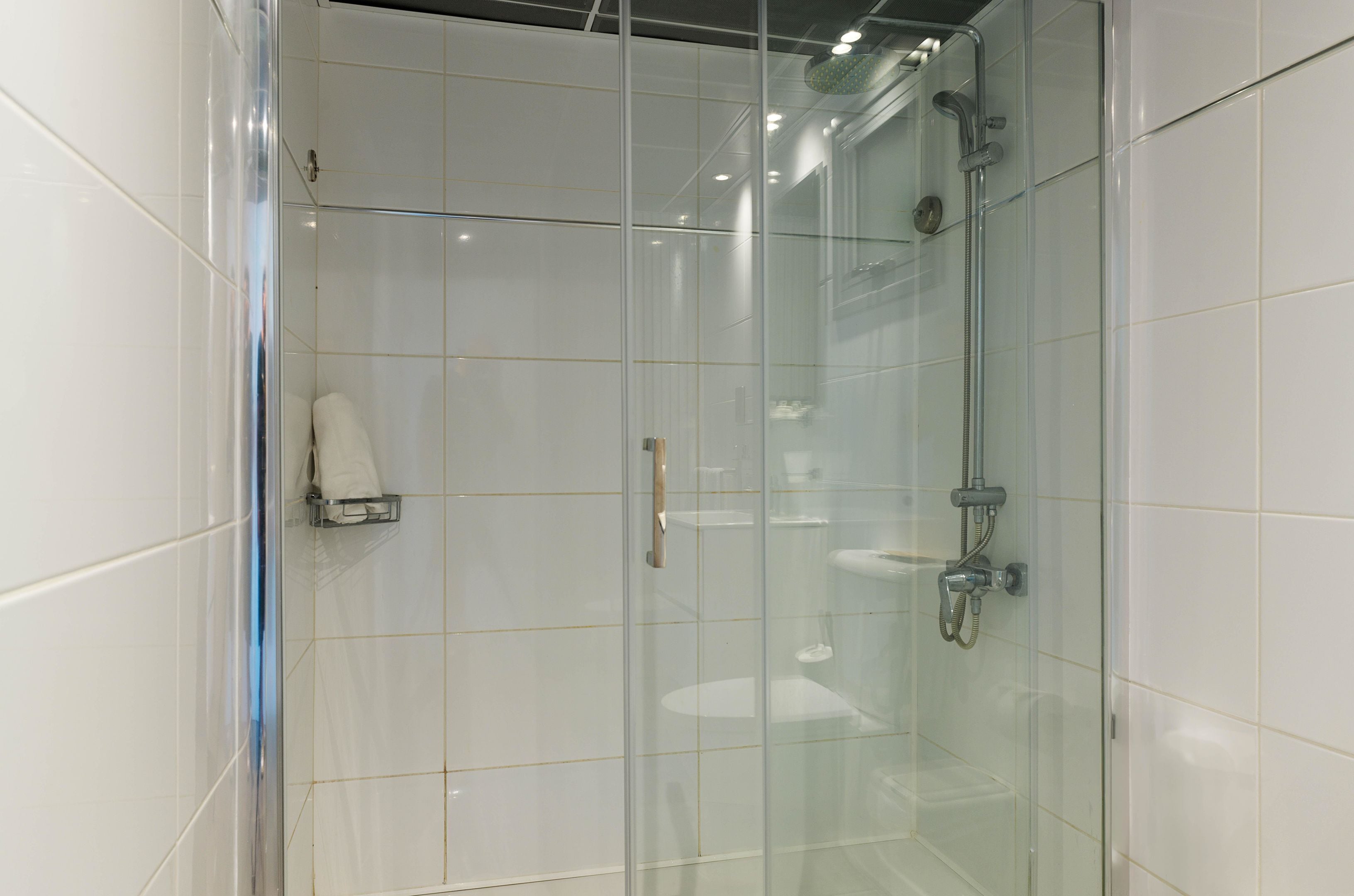 A modern bathroom with a glass shower enclosure, white tiles, and a towel rack.