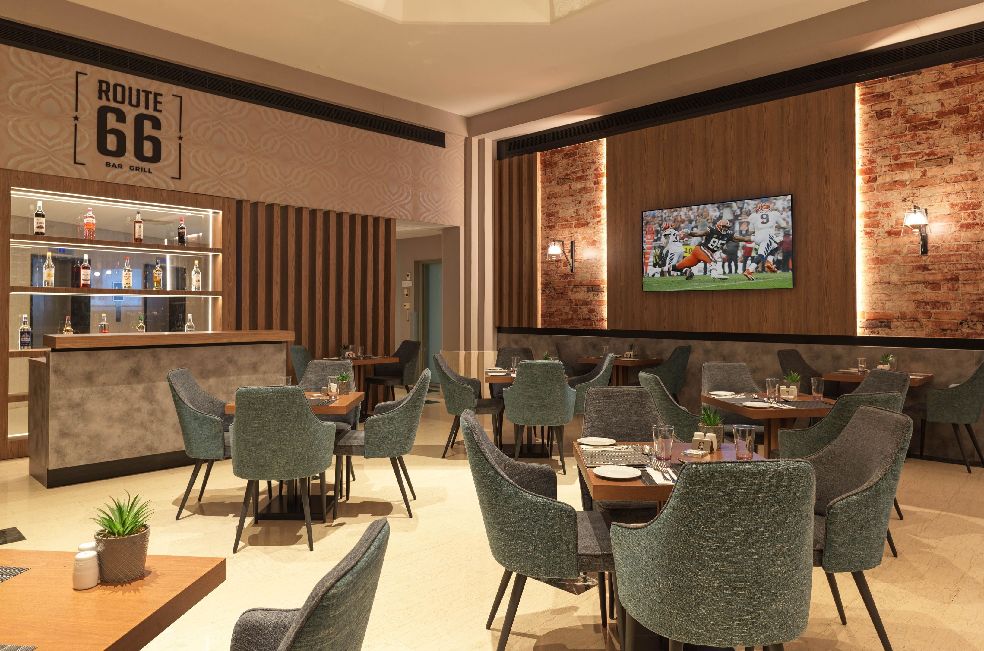 Een restaurant met een bar, bakstenen muren en een televisiescherm waarop een sportwedstrijd wordt vertoond.
