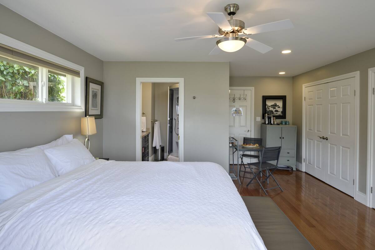 A bedroom with a large bed, a ceiling fan, and a desk with a chair.
