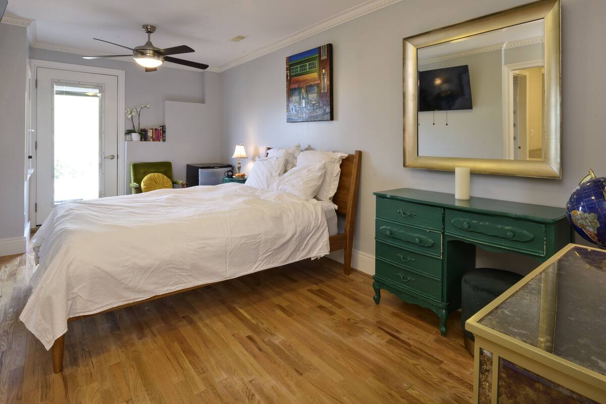 A bedroom with a wooden bed, a green dresser, a ceiling fan, and a large mirror.