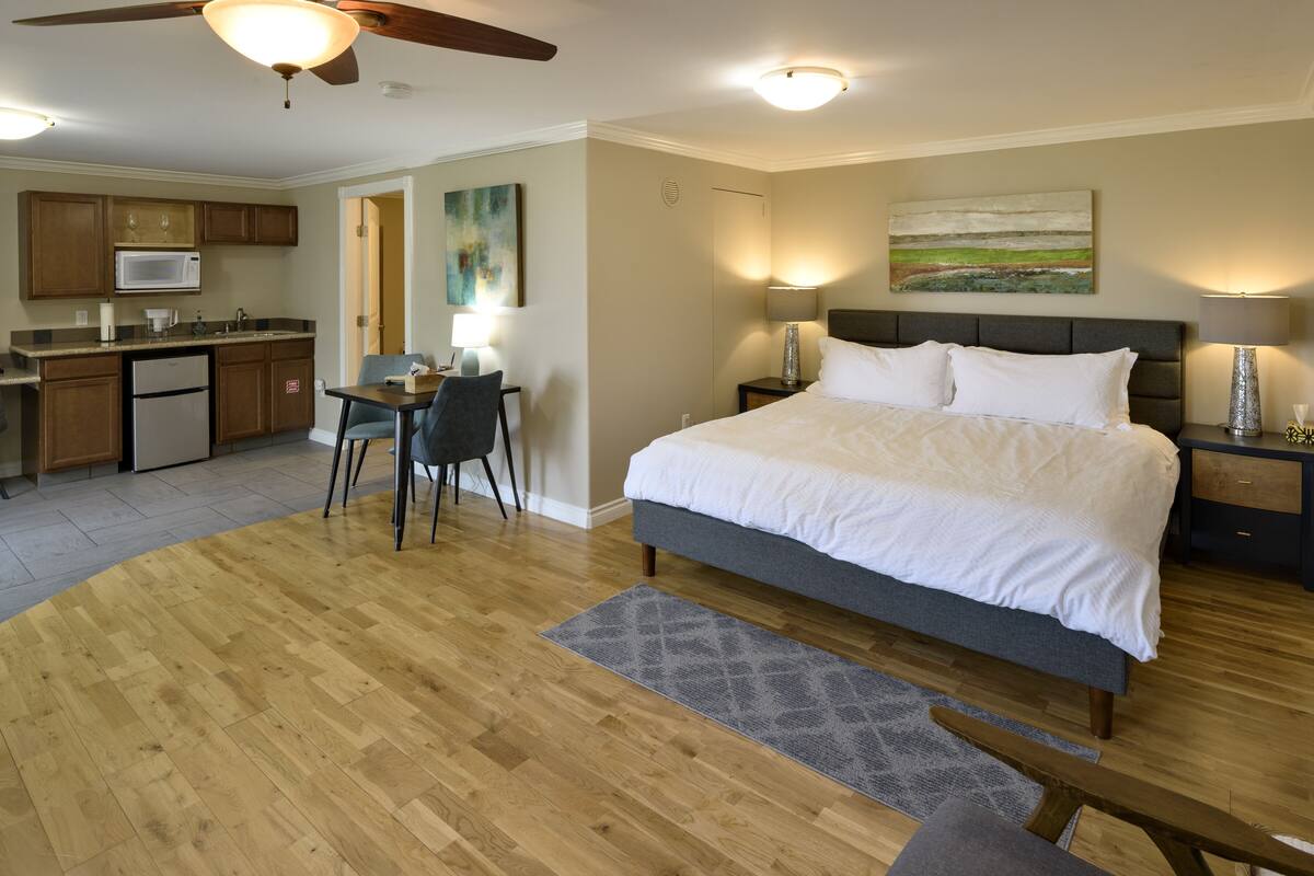 A bedroom with a large bed, a desk, and a kitchenette.