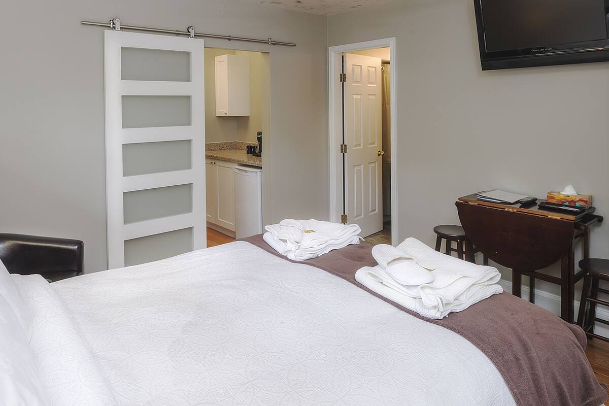 A hotel room with a bed, a desk, a chair, a TV, and a bathroom visible through an open door.