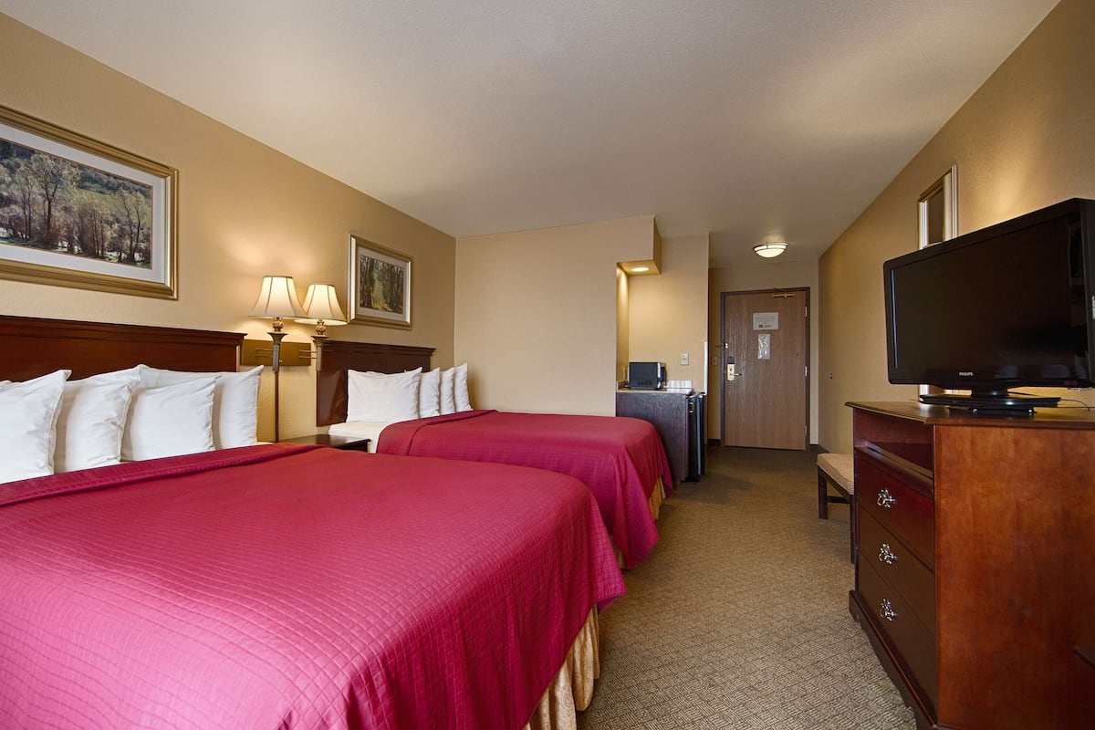 A hotel room with two beds, a television, a desk with a computer, and a door.