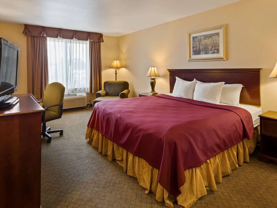 A hotel room with a large bed, two bedside tables with lamps, a desk with a television, a chair, and a window with curtains.