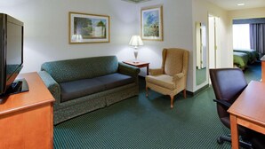 A hotel room with a green patterned sofa, a small armchair, a wooden desk with a television, and two framed pictures on the wall. - Country Inn & Suites by Radisson, Brockton (Boston), MA (Brockton)