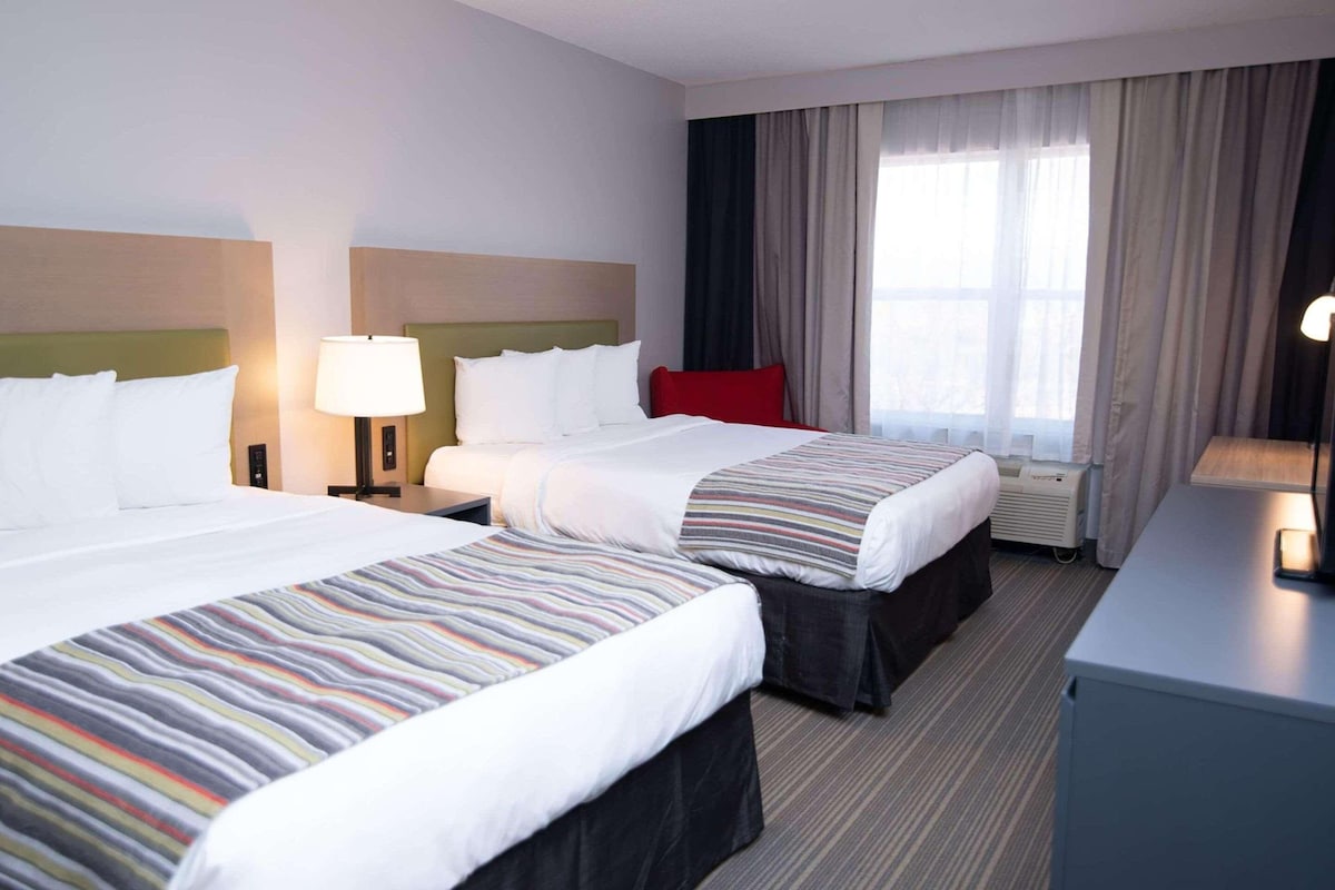 A hotel room with two beds, a desk, a lamp, and a window with curtains.