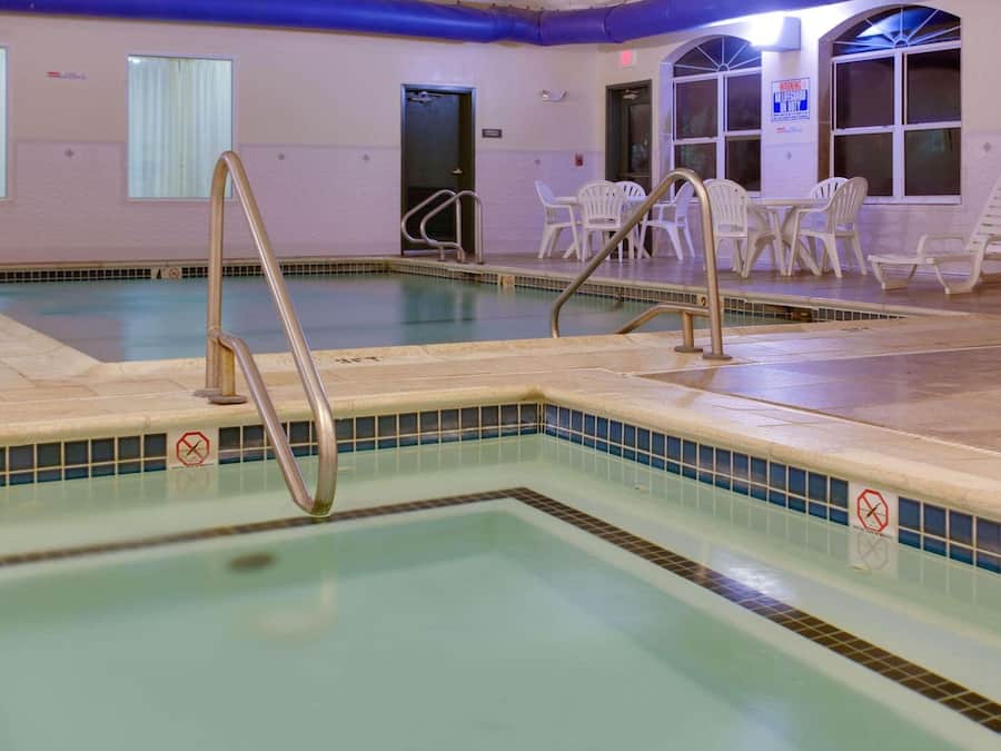An indoor swimming pool with a tiled edge, a no-entry sign, and white plastic chairs around the pool area.