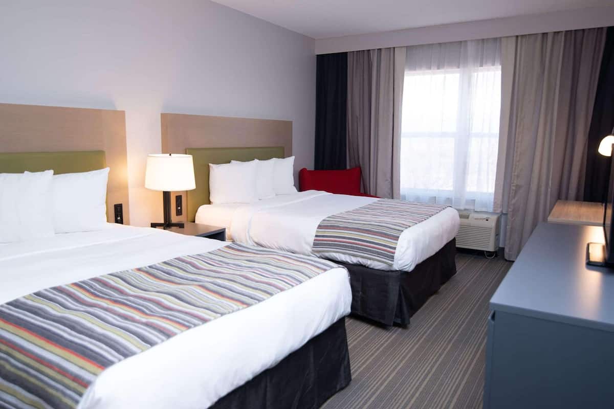 A hotel room with two beds, a desk, a lamp, and a window with curtains.