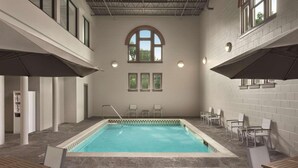 Une piscine intérieure avec un sol carrelé, une grande fenêtre au centre et plusieurs chaises disposées autour de la piscine.