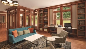 Un salon spacieux avec un canapé bleu, une table basse blanche et un fauteuil à rayures. On y trouve une bibliothèque remplie d’objets décoratifs et un téléviseur posé sur un meuble en bois.