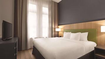 A hotel room with a large bed, a flat-screen TV, a desk, and a lamp.