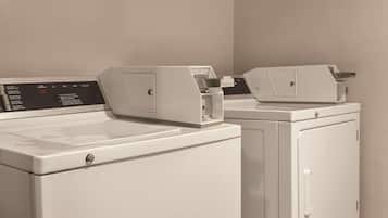 A row of white laundry machines in a room with plain walls.