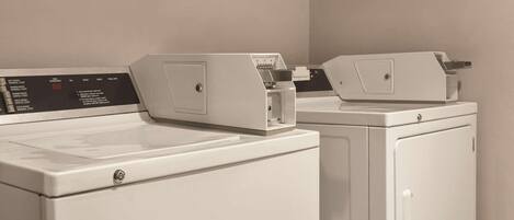 A row of white laundry machines in a room with plain walls.