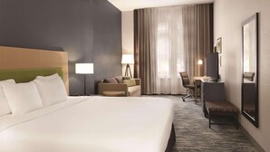 A hotel room with a large bed, a desk, a chair, a sofa, and a small bench.