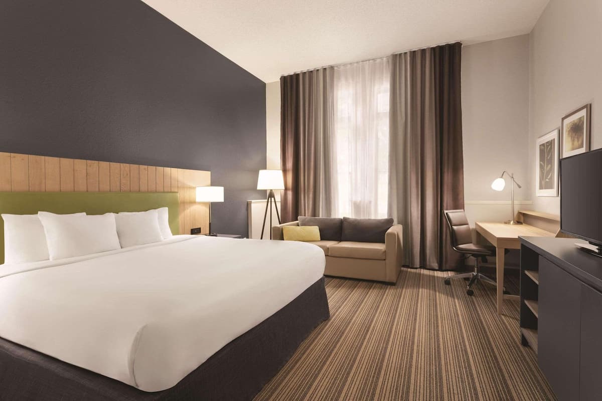 Habitación de hotel con una cama grande, un escritorio, una silla, un sofá y un televisor.