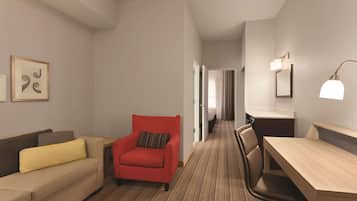 Habitación de hotel con sofá, un sillón rojo, un escritorio y una silla. Se observa un cuadro en la pared y una lámpara sobre el escritorio.