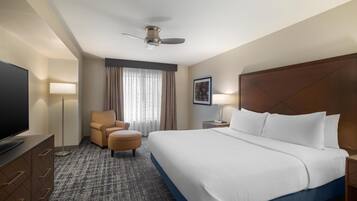 Habitación de hotel con una cama grande, televisión, escritorio, silla, ventilador de techo y ventana con cortinas.