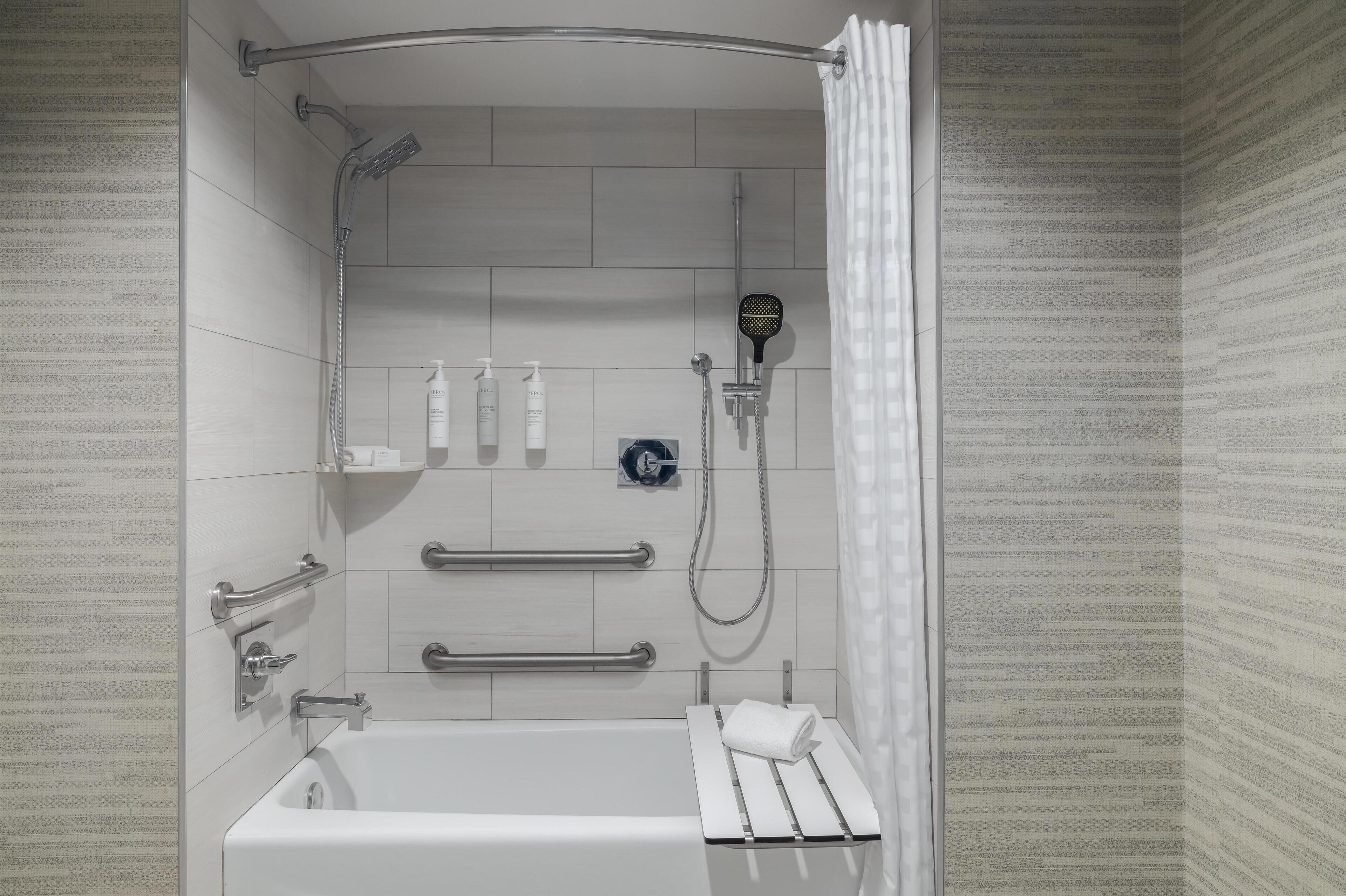 Un área de ducha moderna con ducha de mano, un perchero y una barra de apoyo.
