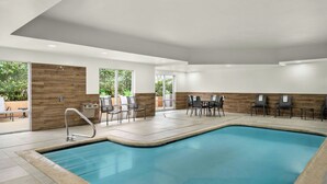Ein moderner, überdachter Schwimmbereich mit großen Glaswänden, einer Wand aus Holz und einer Sitzecke mit Tischen und Stühlen.